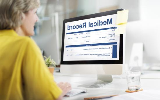 A person in yellow examines medical records on a computer monitor