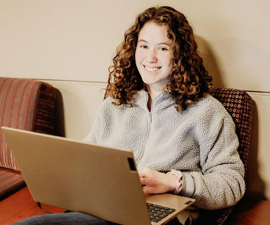 A seated student with a laptop smiles